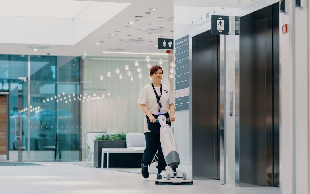 Siivooja siivoaa i-mopilla rakennuksen aulassa.