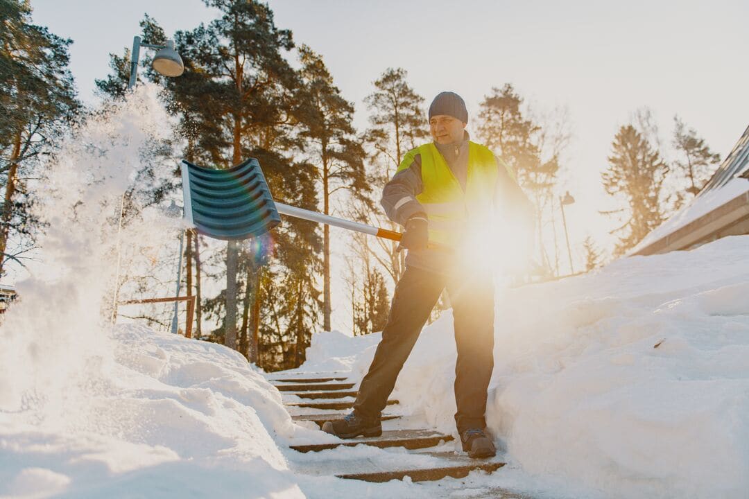 Kiinteistöhoitaja lapioimassa lunta.